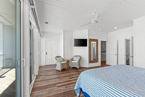 Ein Schlafzimmer mit einem großen Bett, einem Deckenventilator, einem Fernseher und Korbstühlen.