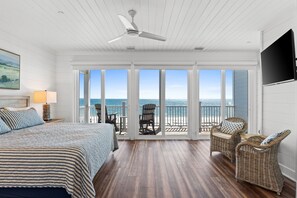 A bedroom with a large bed, a ceiling fan, a view of the ocean through large sliding doors, wicker furniture, and a TV mounted on the wall. - Sailaway Sister- Waterfront & Pet Friendly (Port St. Joe)