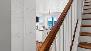 Una cocina moderna con armarios blancos, una escalera de madera y vista al océano.