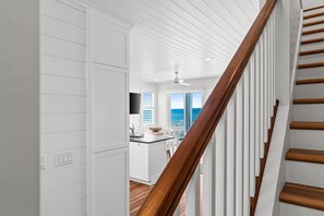 Eine moderne Küche mit weißen Schränken, einer Holztreppe und Blick auf den Ozean.