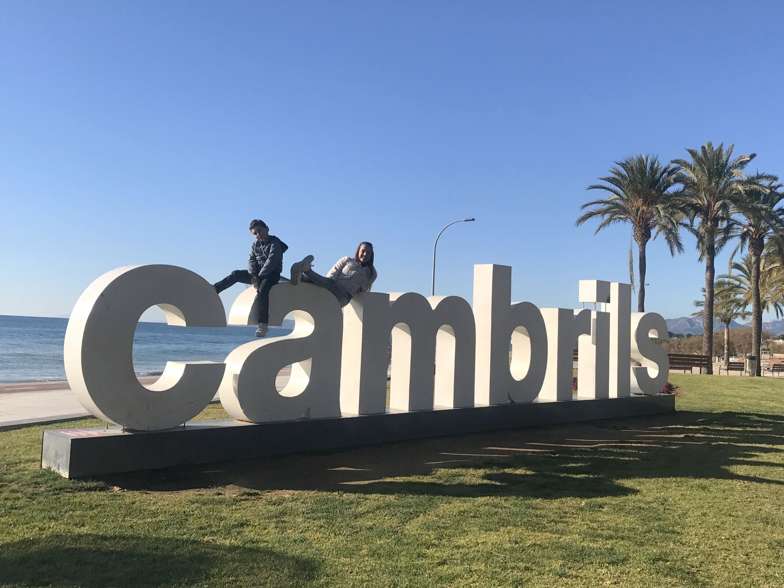 Une grande enseigne extérieure sur laquelle est inscrit le mot « Cambrils » en lettres majuscules, et sur laquelle sont assis deux personnes.