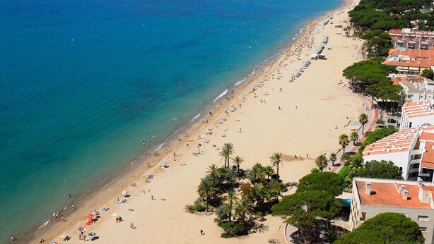 Ein Strand mit einer Reihe von Gebäuden entlang der Küste, Palmen und freiem Blick auf das Meer.