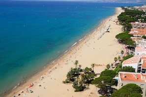 Ein Strand mit einer Reihe von Gebäuden entlang der Küste, Palmen und freiem Blick auf das Meer.
