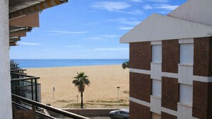 Blick vom Balkon auf einen Sandstrand, eine Palme und ein Gebäude mit Backsteinfassade.