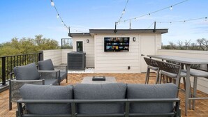 Une terrasse sur le toit, aménagée avec du mobilier d’extérieur, un téléviseur à écran plat et des guirlandes lumineuses.
