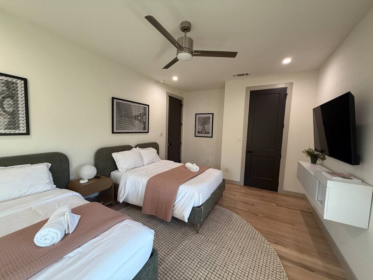 A hotel room with two beds, a ceiling fan, a TV, and a door.