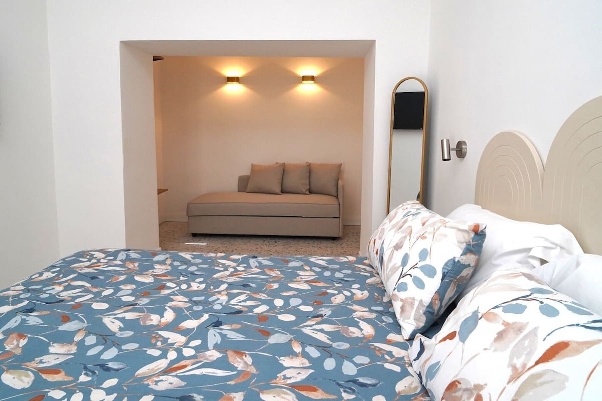 A bedroom with a bed, a sofa, a mirror, and two wall-mounted lights.