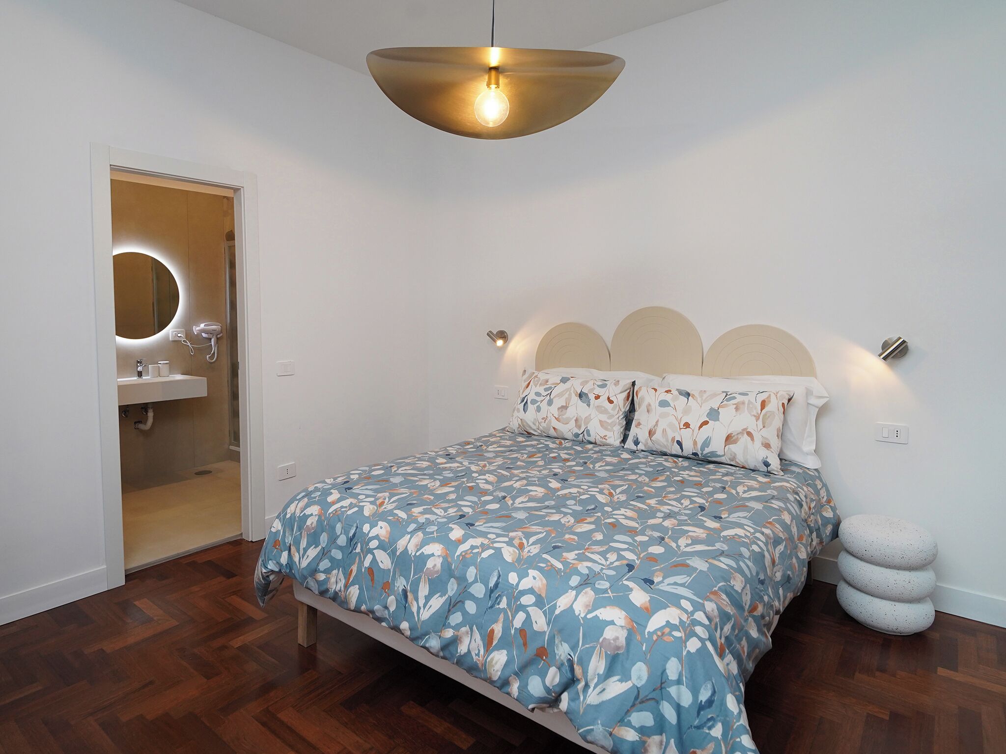 Un dormitorio con cama, lámpara colgante, mesita de noche y luz de pared.