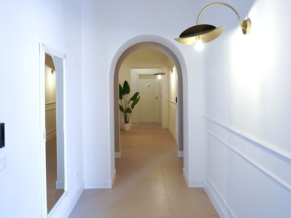 A hallway with white walls, a tiled floor, and a potted plant. - Incoming Medina (Naples)