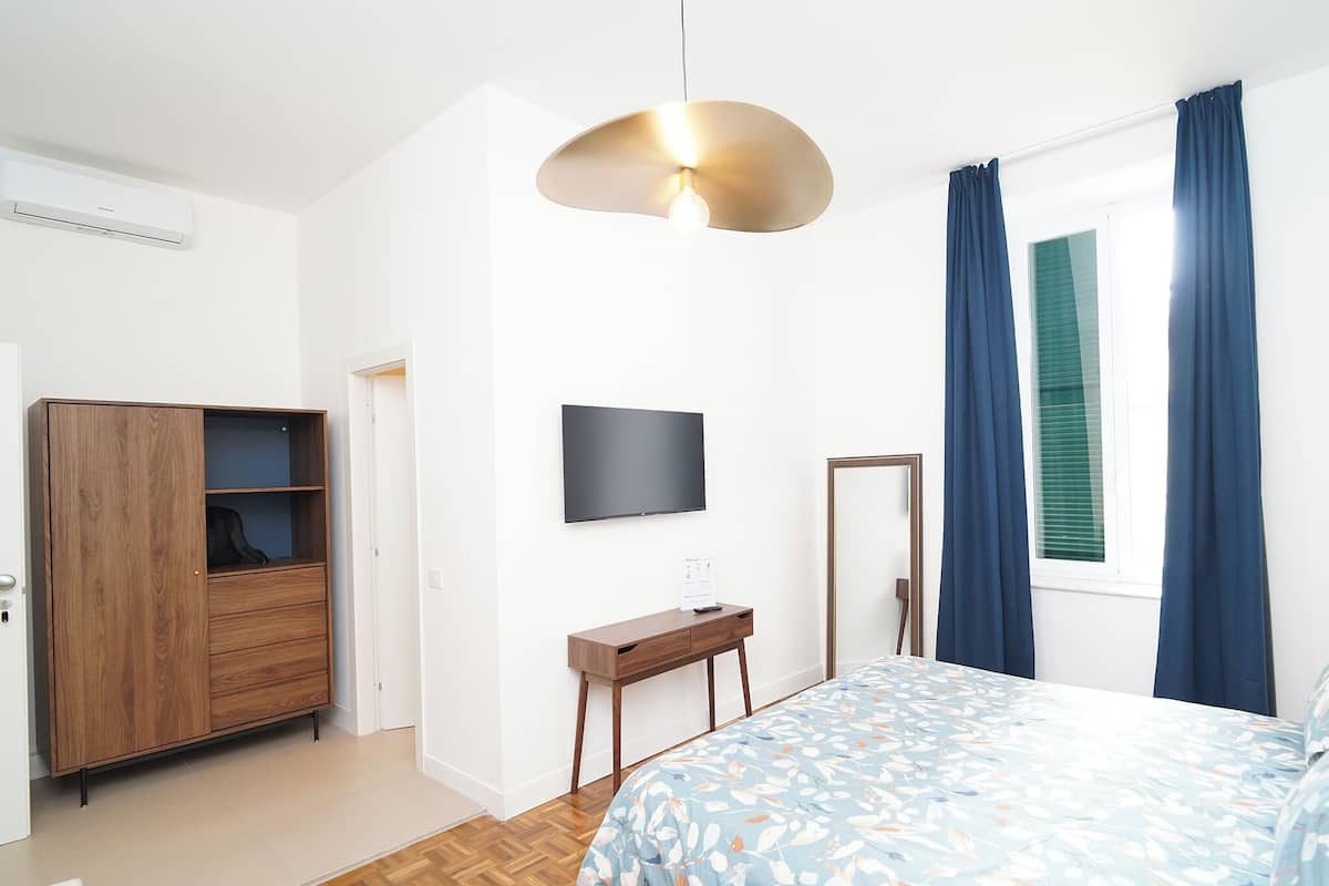A bedroom with a bed, a TV, a wardrobe, a desk, and a window with curtains.