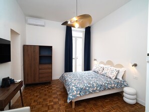 A bedroom with a bed, a wooden wardrobe, a desk with a chair, a television, and a hanging light fixture. - Incoming Medina (Naples)