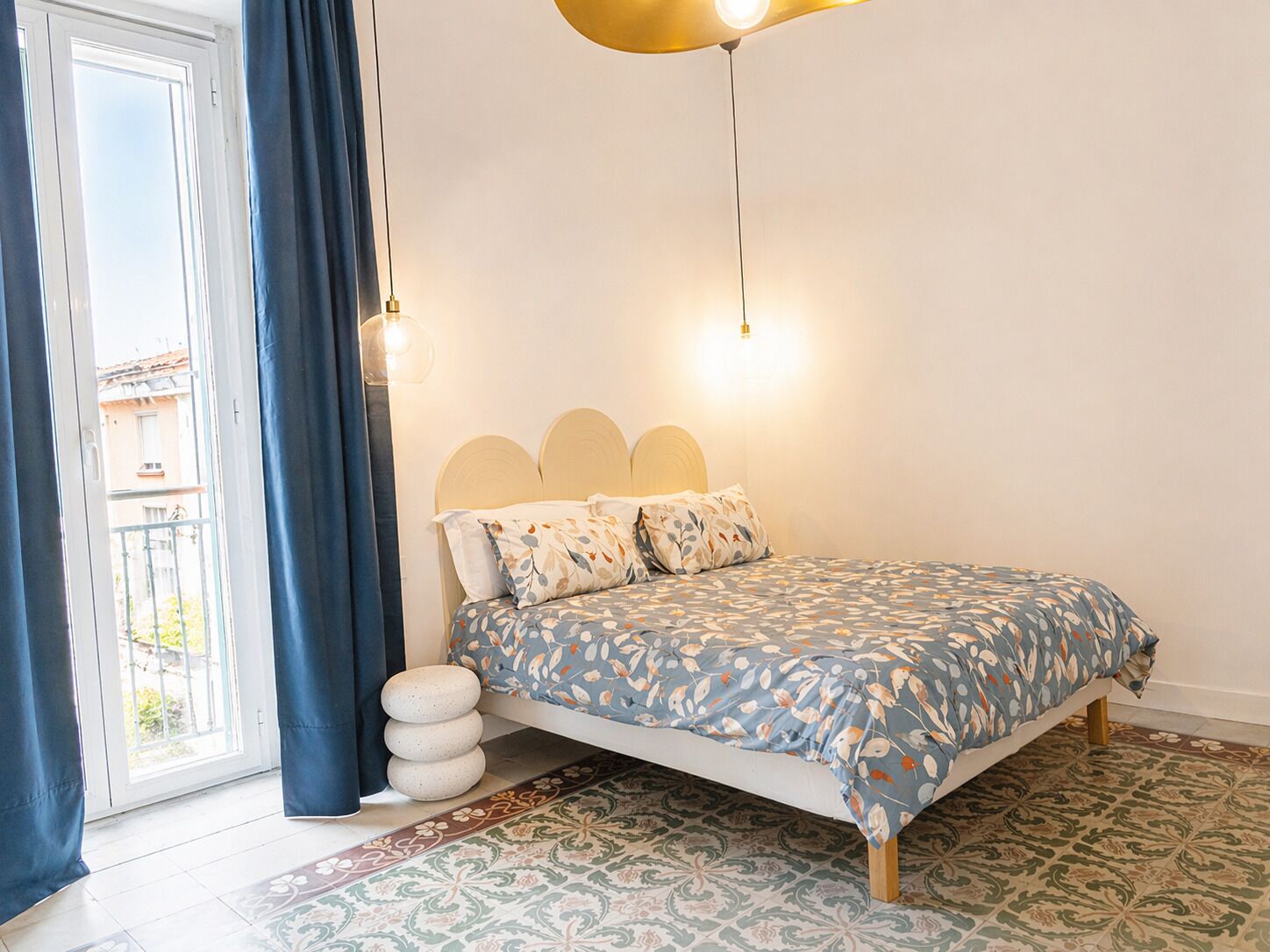 Un dormitorio con cama, cortinas, un tapete estampado y vistas por la ventana.