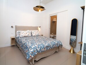 A bedroom with a bed, bedside tables, a hanging light fixture, a mirror, and a door leading to a bathroom. - Incoming Medina (Naples)