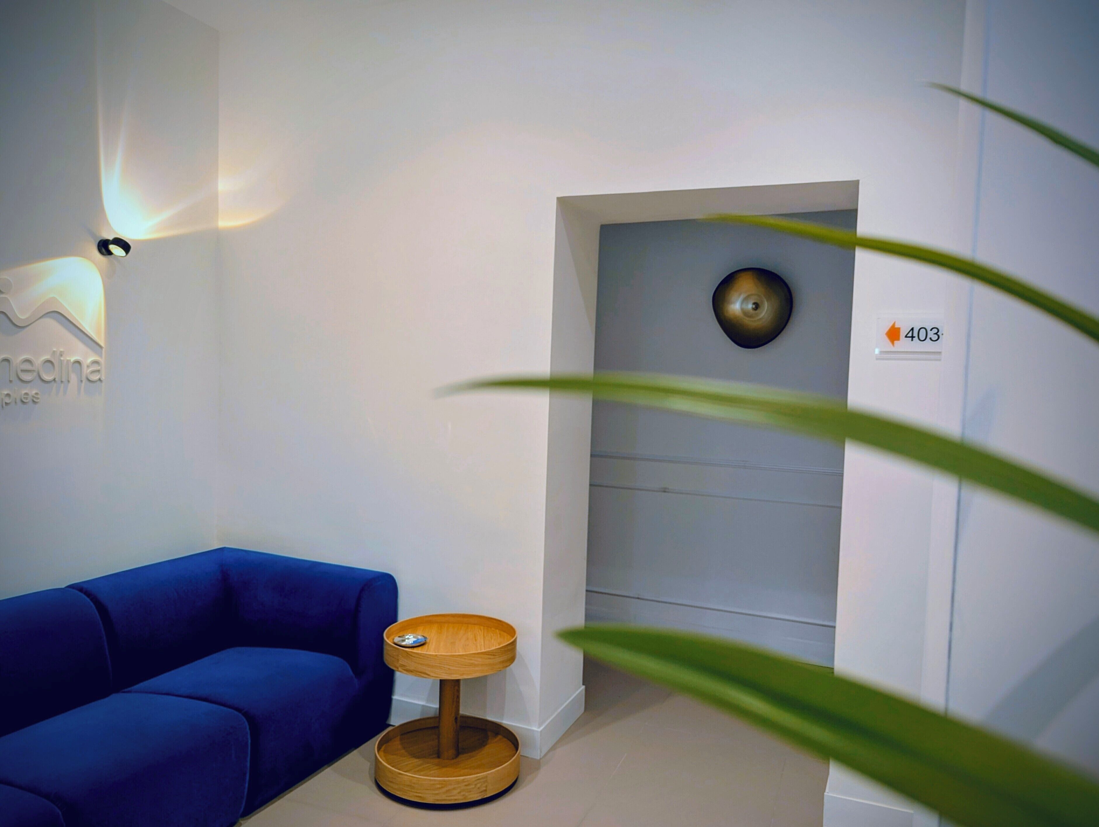 A modern room with a blue sofa, a wooden side table, a wall-mounted light fixture, and a door with a number plate.
