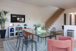 A modern living room with a glass-top dining table, a staircase, and a mounted TV displaying streaming services. - Ultra-Spacious Boutique Retreat in Downtown Dallas (Dallas)