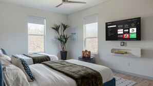 Een slaapkamer met twee bedden, een plafondventilator, een aan de muur bevestigde televisie met streamingdiensten, en een plant.