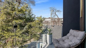 Een balkon met een stoel, planten in potten en uitzicht op gebouwen.