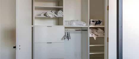 Un vestidor amplio con estantes múltiples, espacio para colgar ropa y un perchero con prendas dobladas.