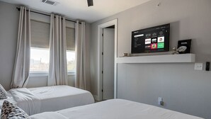 Une chambre d’hôtel avec deux lits, un téléviseur fixé au mur et une fenêtre avec des rideaux.