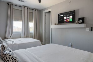 Ein Hotelzimmer mit zwei Betten, einem an der Wand befestigten Fernseher und einem Fenster mit Vorhängen.