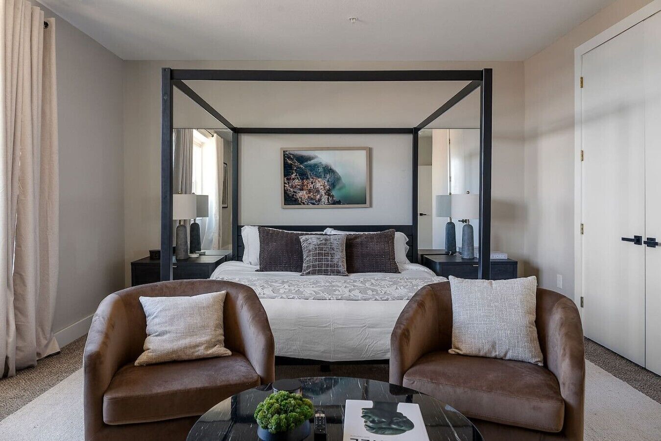A hotel room with a four-poster bed, two armchairs, a coffee table, and a painting on the wall.