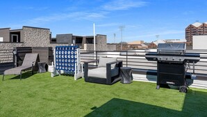 Une terrasse sur le toit équipée d’un barbecue, de sièges et d’un élément décoratif aquatique bleu.