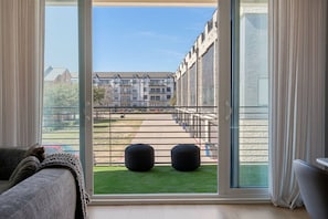 A room with a large window, a view of a building, and a green lawn outside. - Elevated Modern Rooftop Oasis In Prime Dallas (Farmers Branch)