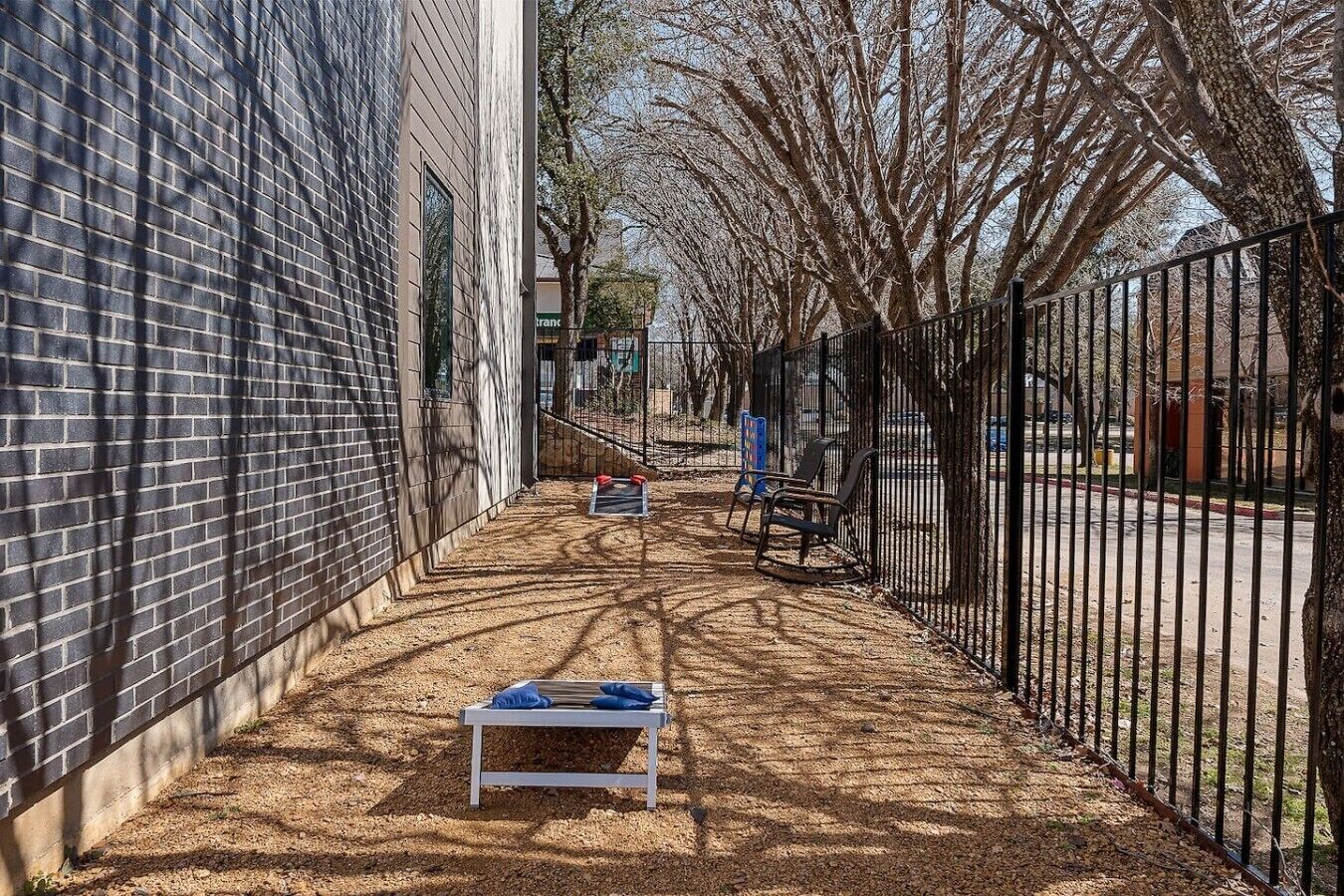 A narrow alley with a brick wall on one side and a metal fence on the other, leading to a bench and a sign.