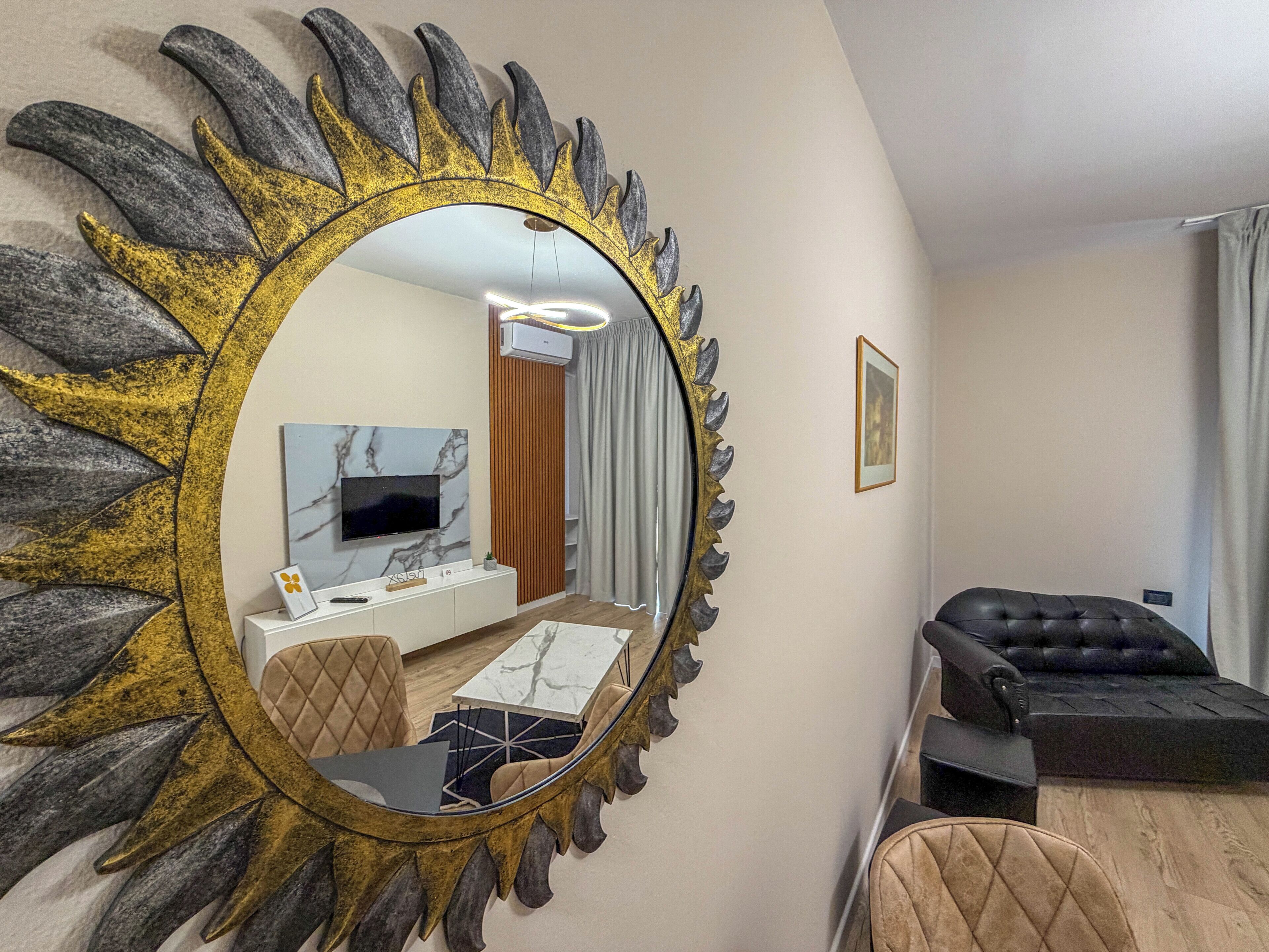 A sunburst mirror, a television on a marble wall, a sofa, and a dining area with a table and chairs.