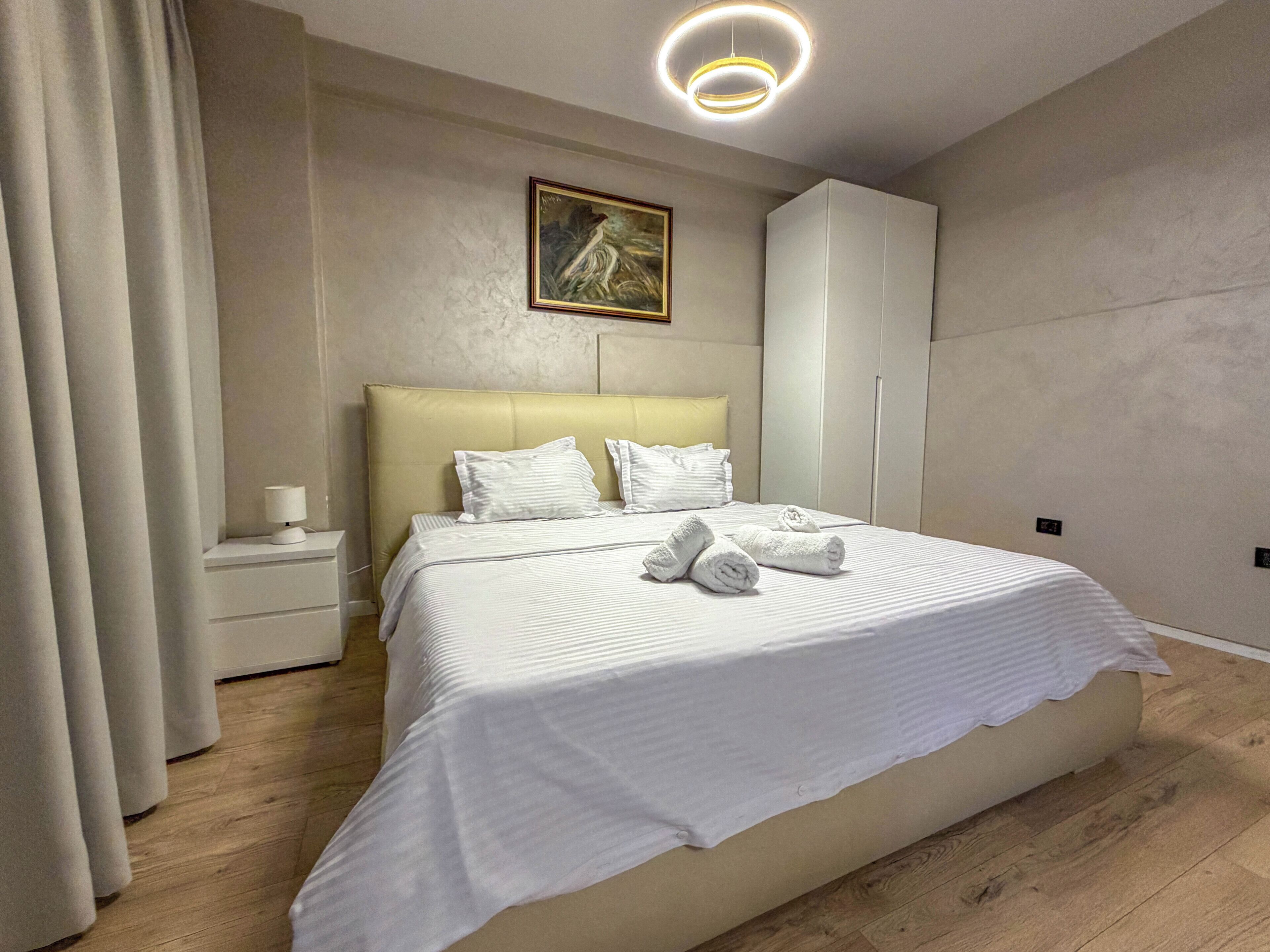 Una habitación de hotel moderna con una cama grande, una mesita de noche, un armario y un cuadro en la pared.