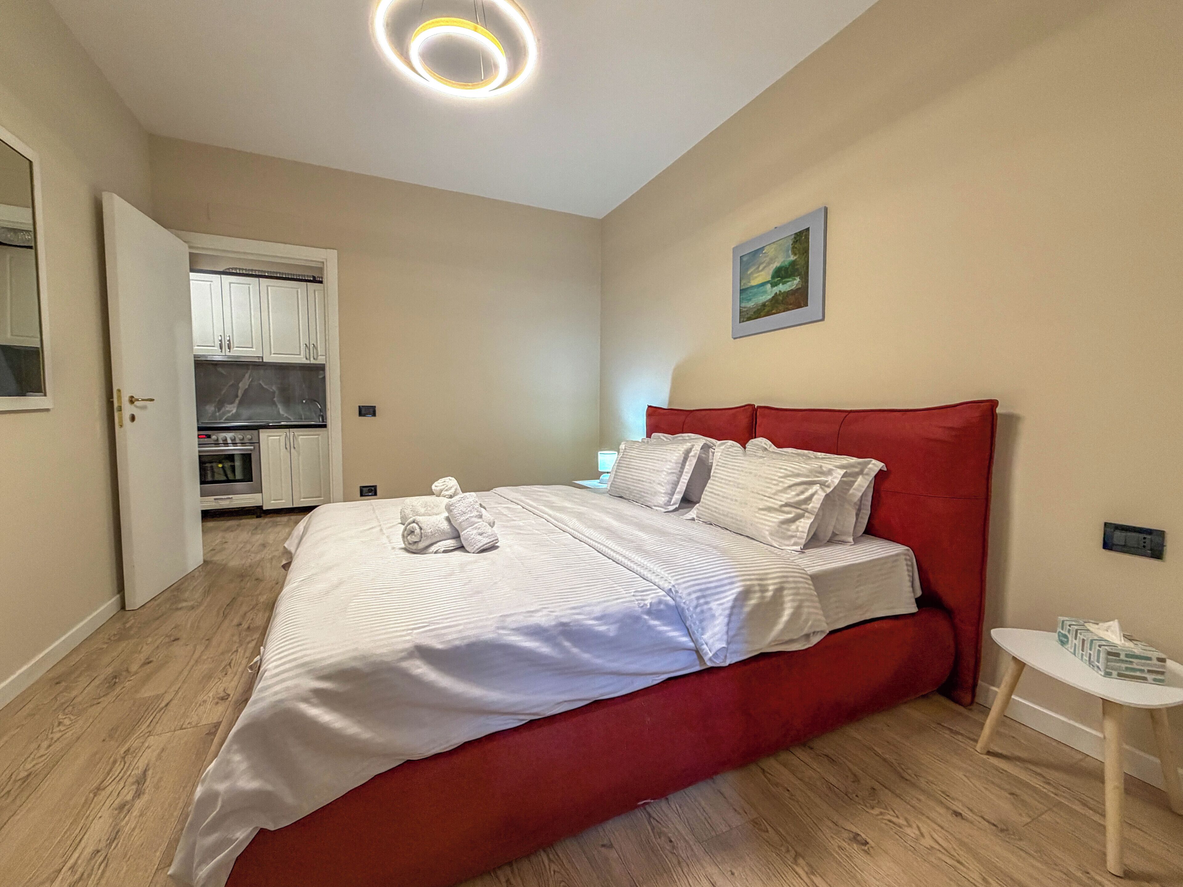 A bedroom with a red bed, white bedding, a small bedside table, and a painting on the wall.