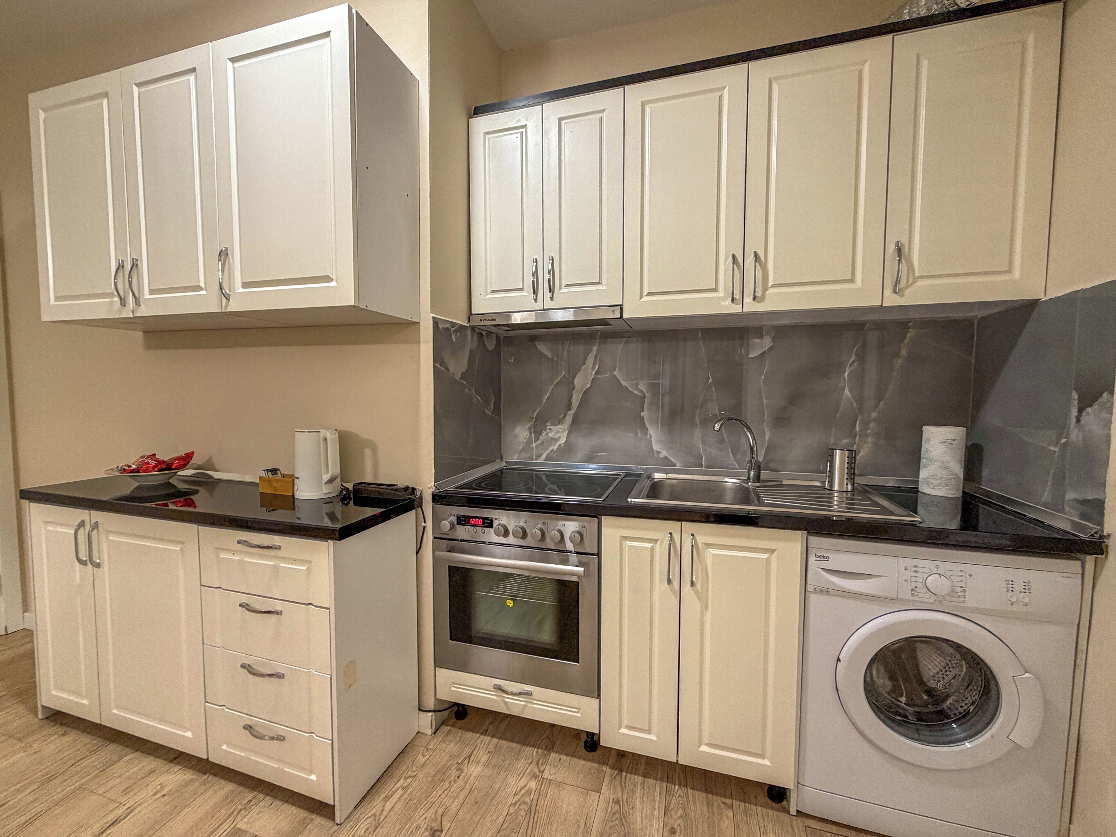 A compact kitchen with white cabinets, a stove, oven, sink, and a washing machine.
