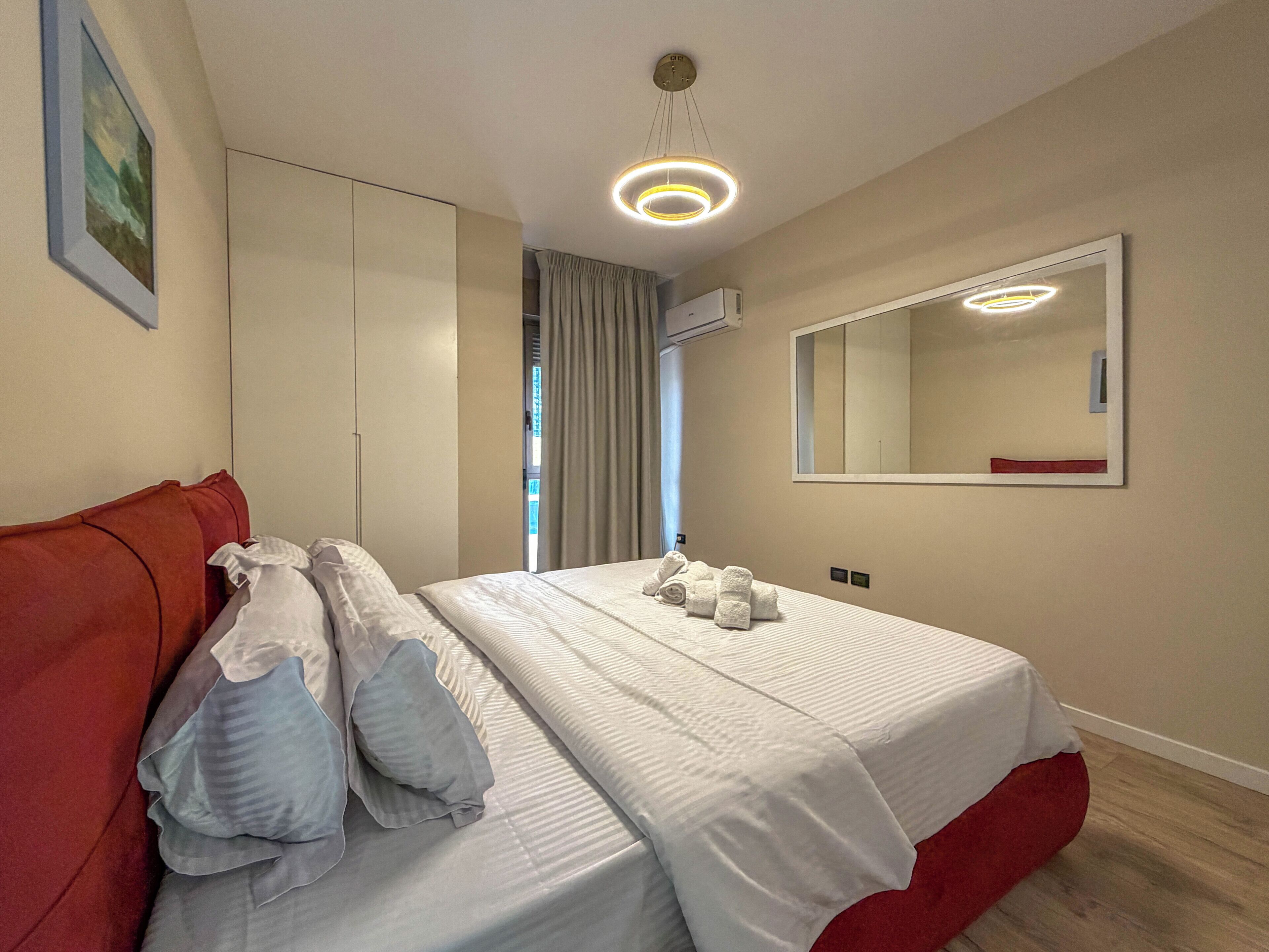 Una habitación de hotel con cama, sofá rojo, un espejo grande y una lámpara en el techo.