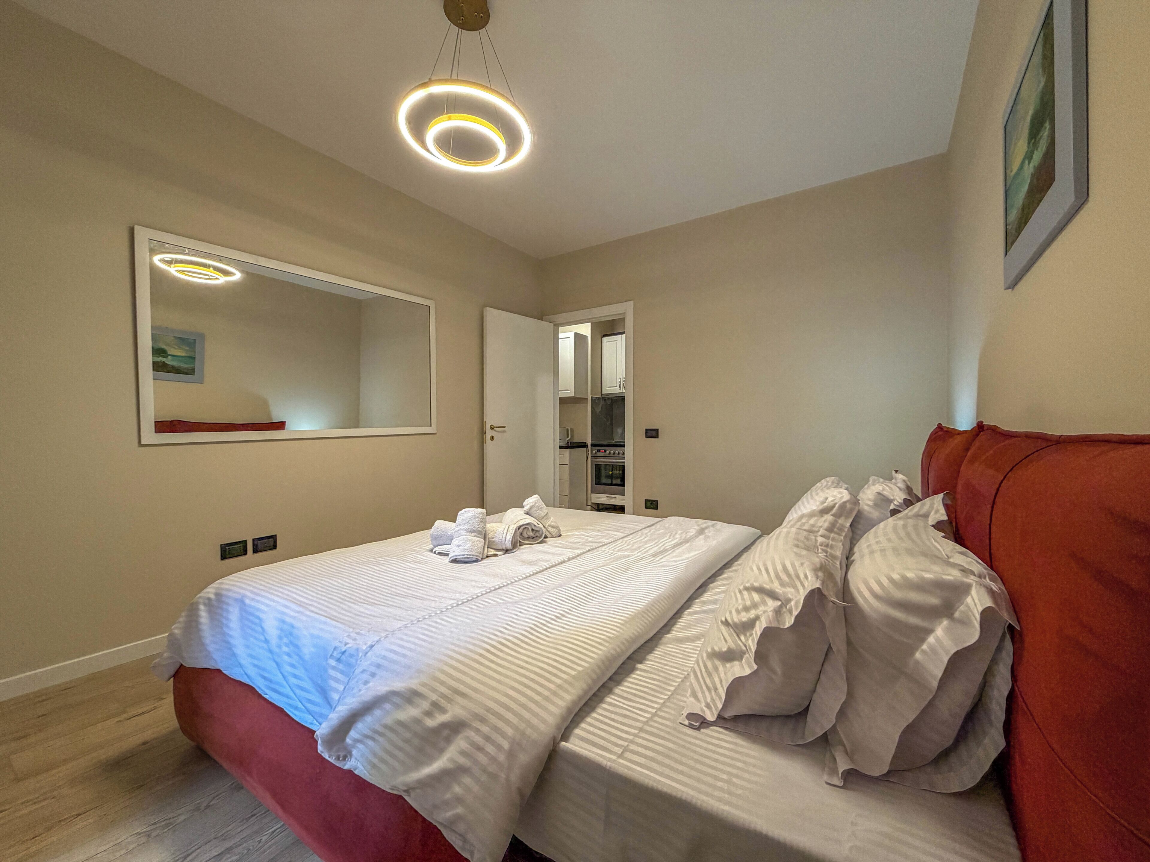 Een hotelkamer met een tweepersoonsbed, een rode hoofdbord, een grote spiegel en een plafondlamp.