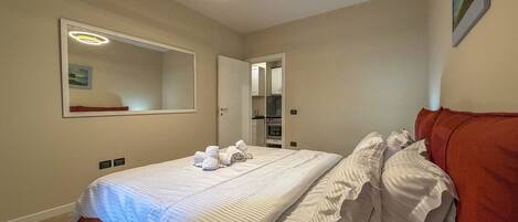 A hotel room with a double bed, a red headboard, a large mirror, and a ceiling light fixture.