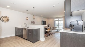 A modern kitchen with a central island, built-in appliances, pendant lighting, and a dining area with a view. - New Coastal Condo - Walk to Shops + Bike to Beach (Rehoboth Beach)