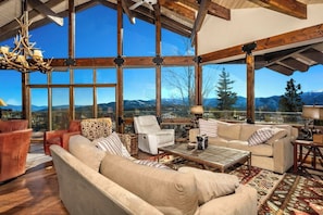 A spacious living area with a large window offering a mountain view, a chandelier, and a variety of seating options.
