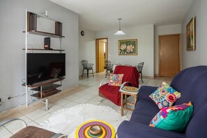 A living room with a TV, sofa, and dining area. - Apartamento com 3 quartos e Garagem no Setor Bueno (Goiânia)