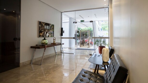 Eine Lobby mit Glastür zum Außenbereich, einer Bank, einem kleinen Tisch mit einer Vase und einem Gemälde an der Wand.