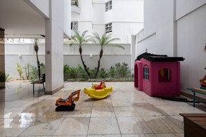A courtyard with a play area, a small pink playhouse, and a toy excavator. - Apartamento com 3 quartos e Garagem no Setor Bueno (Goiânia)