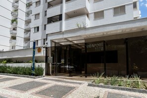 A modern building with a glass entrance, a sign reading 'GUAPORÉ 1178', and a paved area with plants. - Apartamento com 3 quartos e Garagem no Setor Bueno (Goiânia)