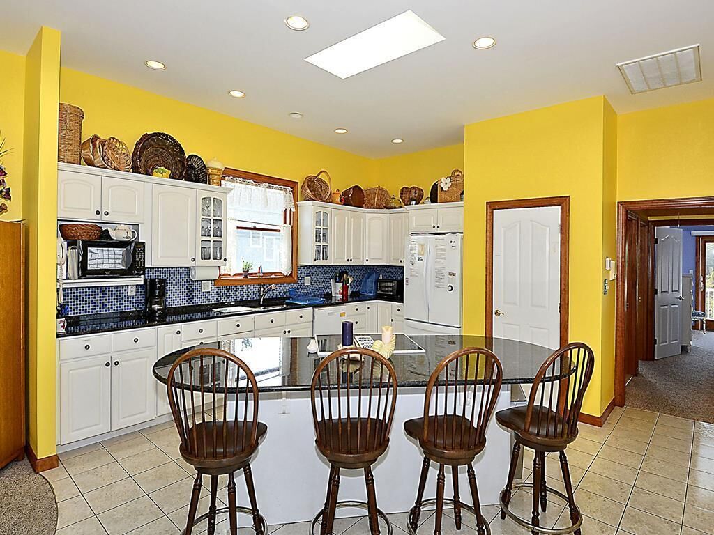 A kitchen with white cabinets, a central island with chairs, and a yellow wall.