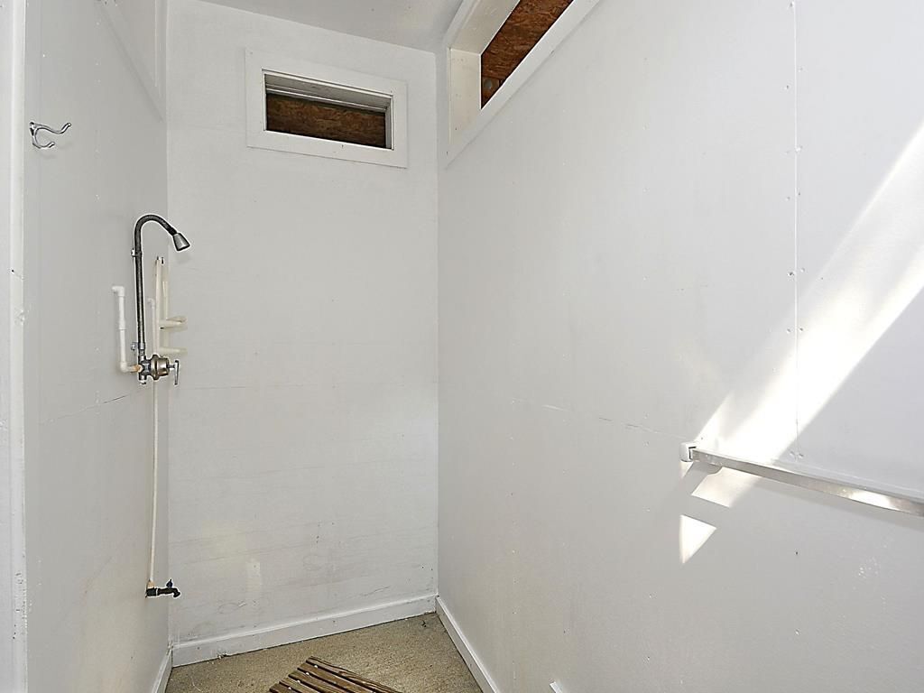 Un baño pequeño con paredes blancas, ducha, ventana y puerta.