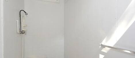 Un baño pequeño con paredes blancas, ducha, ventana y puerta.