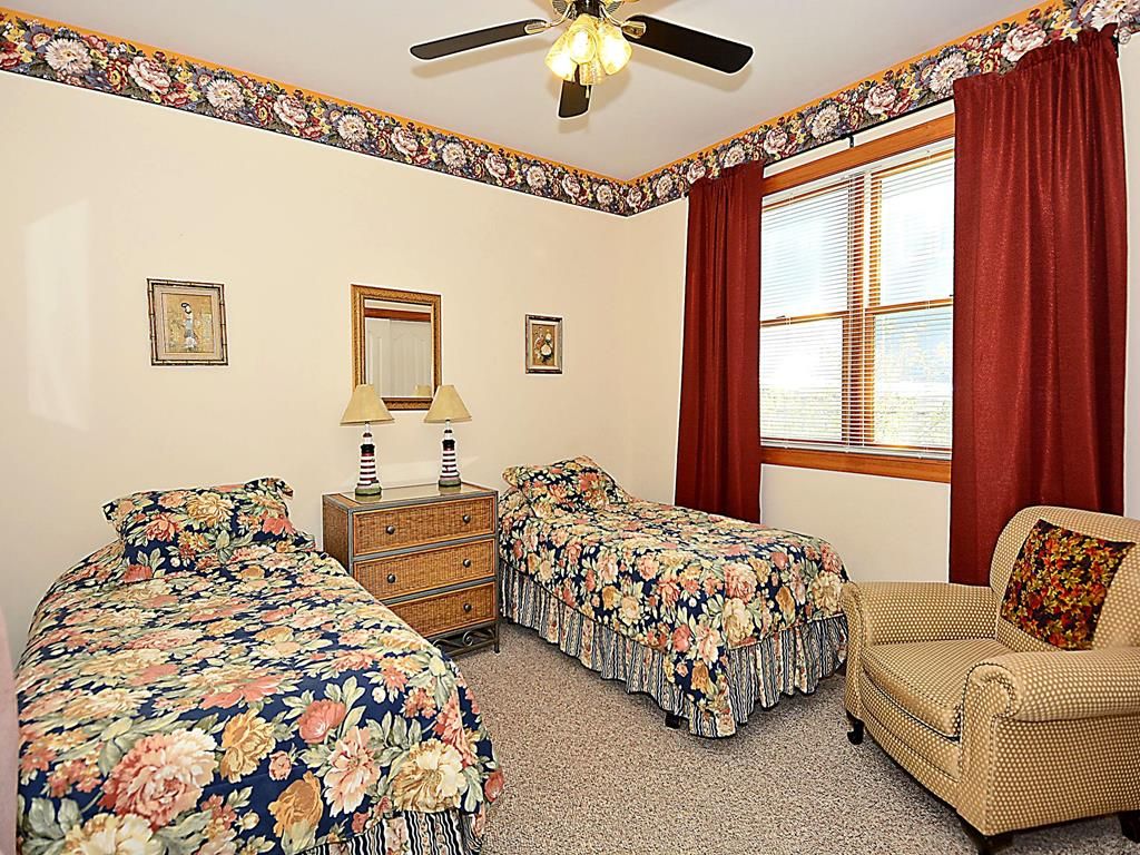 A bedroom with two single beds, a dresser, a chair, and a window with curtains.