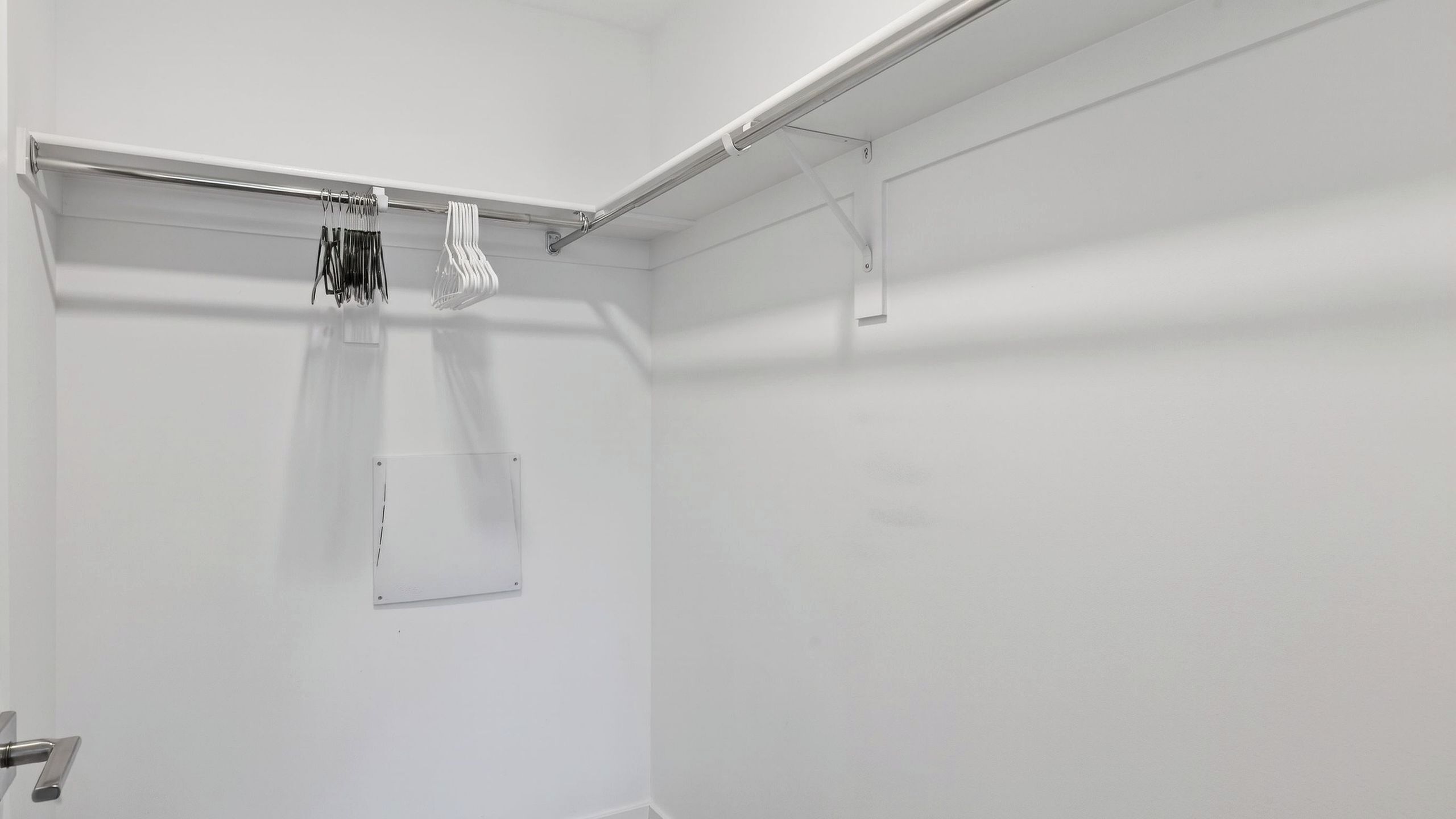 A white closet with a metal rod for hanging clothes, a small window, and a door with a handle.
