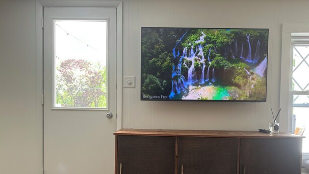A television mounted on a wall above a wooden cabinet with a door.