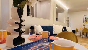 Una sala de estar moderna con comedor, que incluye una bandeja azul con el texto 'HAPPY HOME', una taza amarilla y un jarrón con flores blancas.
