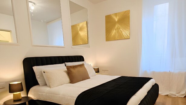 Un dormitorio con cama, mesitas de noche, un espejo y una ventana con cortinas.