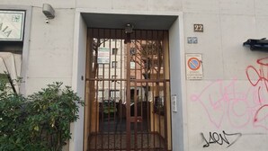 Entrada de un edificio con una reja metálica, un cartel que indica zona de no estacionamiento y grafitis en la pared.